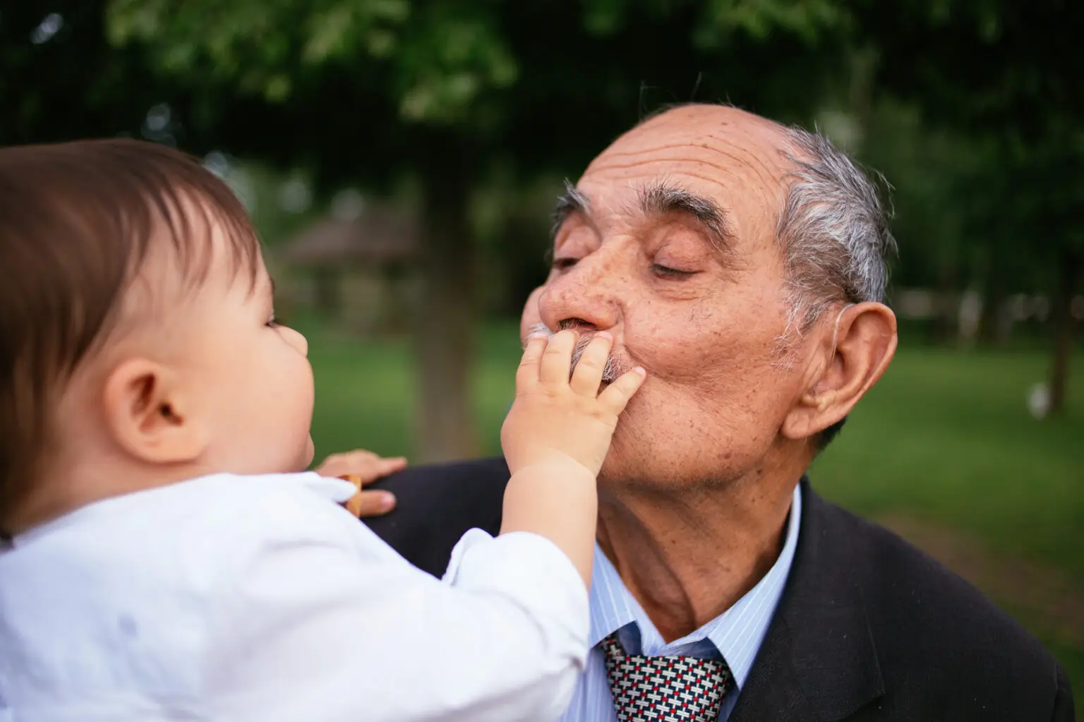 Elderly man in suit holding infant outdoors in garden