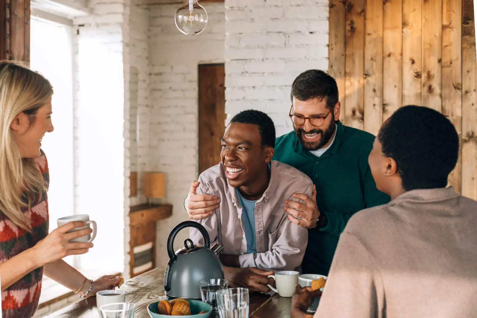 Four friends laughing together around kitchen table with coffee